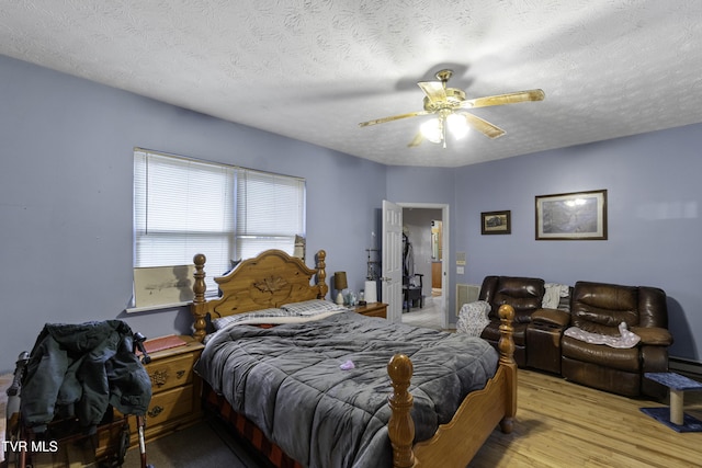 bedroom with ceiling fan, light hardwood / wood-style floors, and a textured ceiling