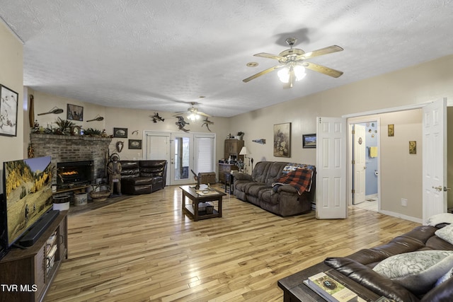 living room with french doors, a brick fireplace, a textured ceiling, ceiling fan, and light hardwood / wood-style flooring