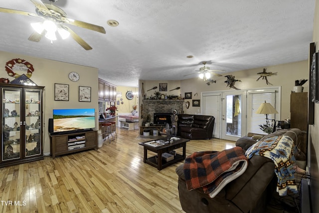 living room featuring a textured ceiling, light hardwood / wood-style floors, a brick fireplace, and ceiling fan