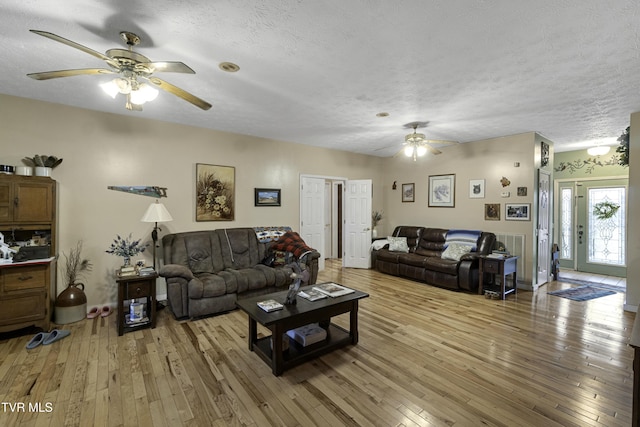 living room featuring ceiling fan, light hardwood / wood-style flooring, and a textured ceiling