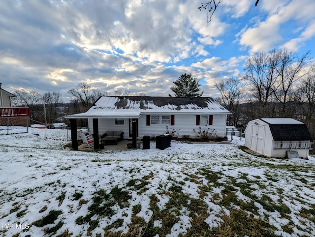 snow covered rear of property featuring a shed