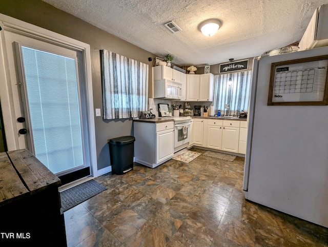 kitchen featuring white appliances, white cabinetry, and a textured ceiling