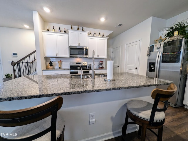 kitchen featuring appliances with stainless steel finishes, dark stone counters, dark wood-type flooring, decorative backsplash, and white cabinets