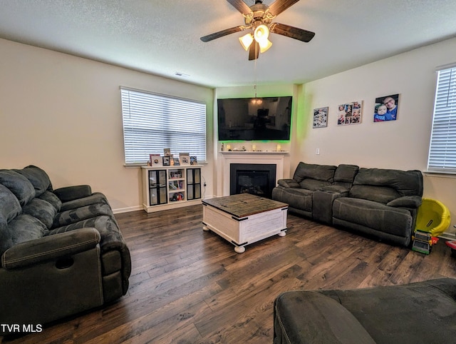 living room featuring dark wood-type flooring, a textured ceiling, ceiling fan, and a healthy amount of sunlight