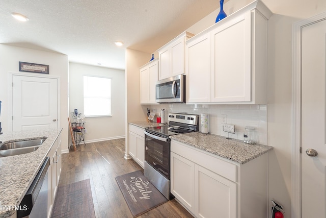 kitchen featuring backsplash, light stone countertops, dark hardwood / wood-style flooring, white cabinetry, and stainless steel appliances