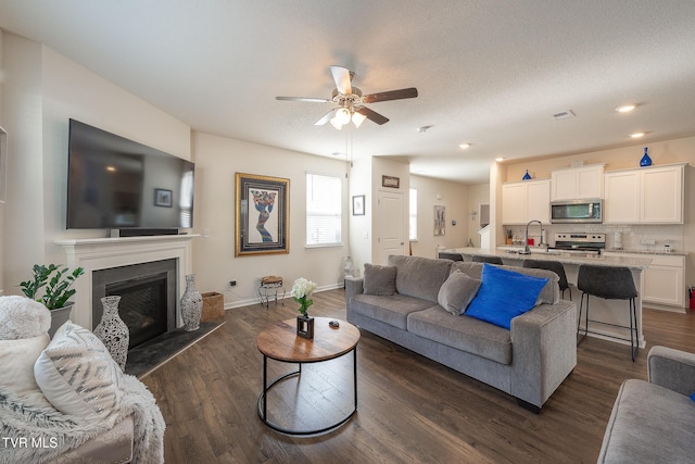 living room with a textured ceiling, ceiling fan, dark wood-type flooring, and sink