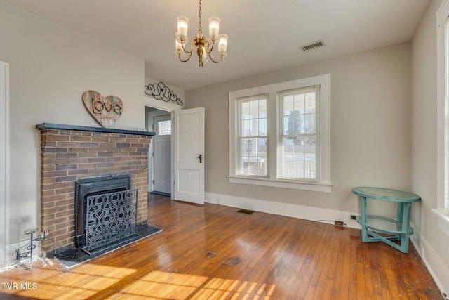 living room with a brick fireplace, hardwood / wood-style flooring, and an inviting chandelier