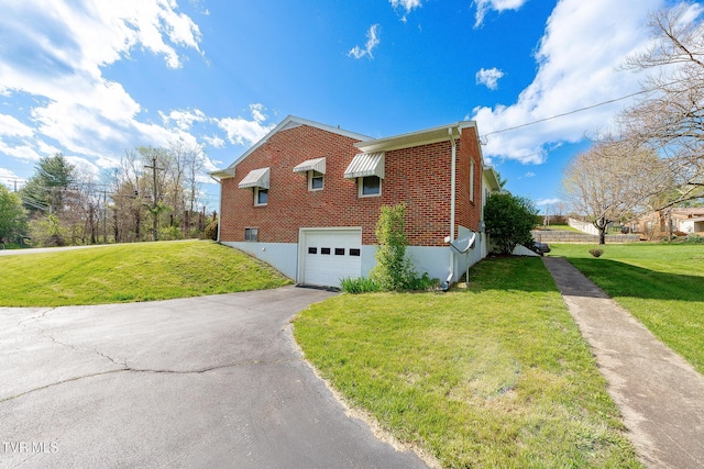 view of side of property featuring brick siding, aphalt driveway, a garage, and a lawn