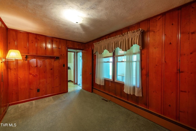 carpeted empty room featuring wooden walls, a baseboard heating unit, and a textured ceiling