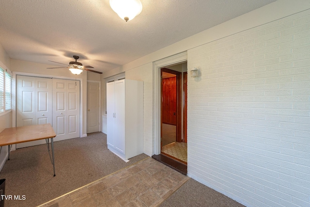 unfurnished bedroom featuring a textured ceiling, ceiling fan, dark colored carpet, and multiple closets
