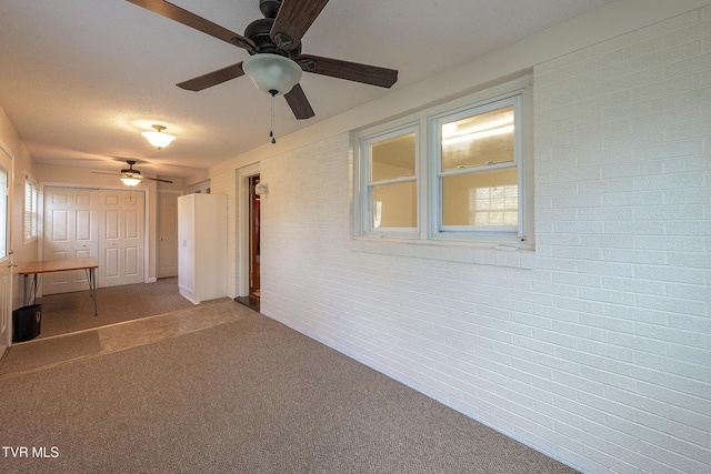 interior space with a textured ceiling, a ceiling fan, brick wall, and a healthy amount of sunlight