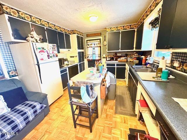 kitchen with sink, light parquet flooring, white fridge, and a textured ceiling