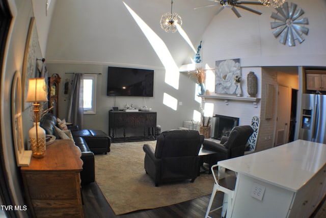 living room featuring dark wood-type flooring, a brick fireplace, ceiling fan with notable chandelier, and high vaulted ceiling