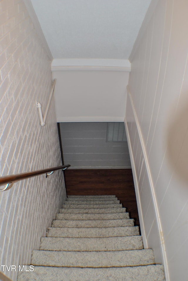 staircase featuring hardwood / wood-style flooring, crown molding, and wood walls