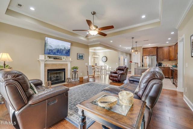 living room featuring light hardwood / wood-style flooring, ceiling fan, a tray ceiling, a fireplace, and ornamental molding