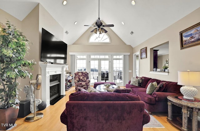 living room with high vaulted ceiling, french doors, ceiling fan, a fireplace, and light hardwood / wood-style floors