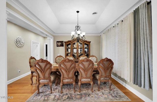 dining area with hardwood / wood-style flooring, a notable chandelier, and a tray ceiling