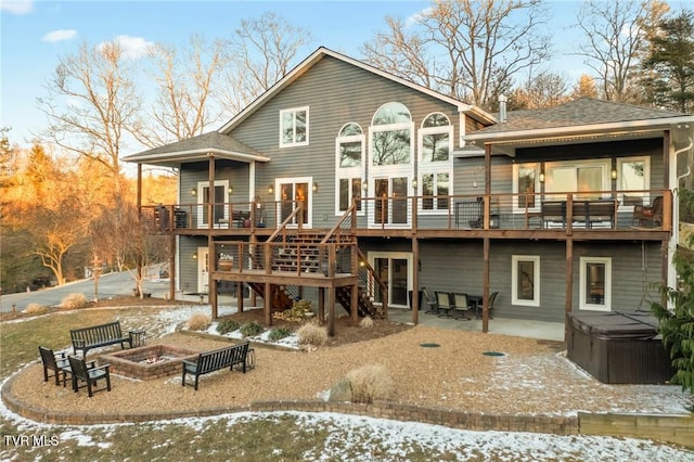 snow covered back of property with a patio, a hot tub, a fire pit, and a wooden deck