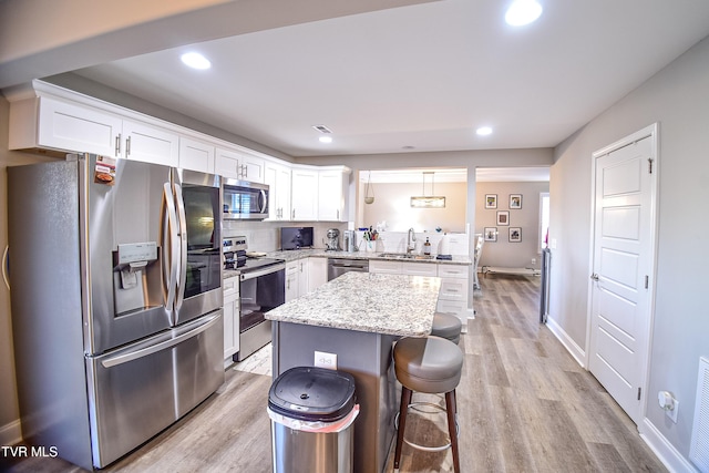 kitchen featuring pendant lighting, stainless steel appliances, a kitchen island, white cabinetry, and sink