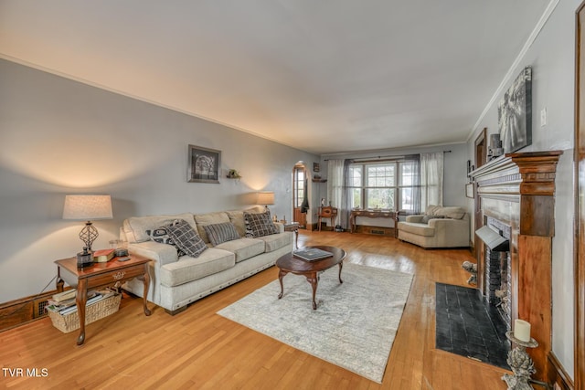 living room with a tiled fireplace, crown molding, and light hardwood / wood-style flooring