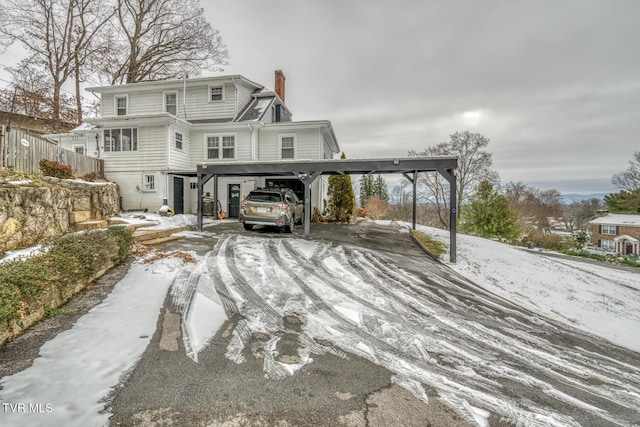 snow covered house featuring a carport