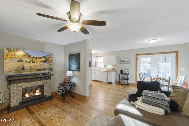 living room featuring ceiling fan, sink, a stone fireplace, and light wood-type flooring