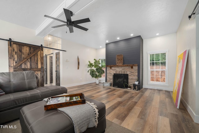 living room featuring a barn door, wood-type flooring, beamed ceiling, ceiling fan, and a fireplace