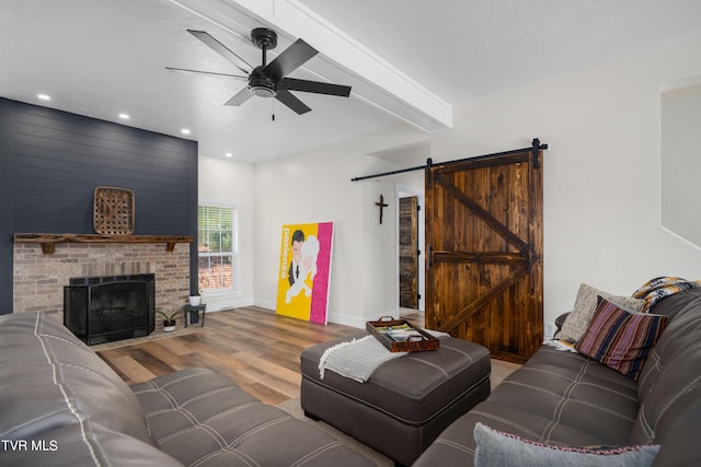 living room with a barn door, ceiling fan, a fireplace, beam ceiling, and light hardwood / wood-style flooring