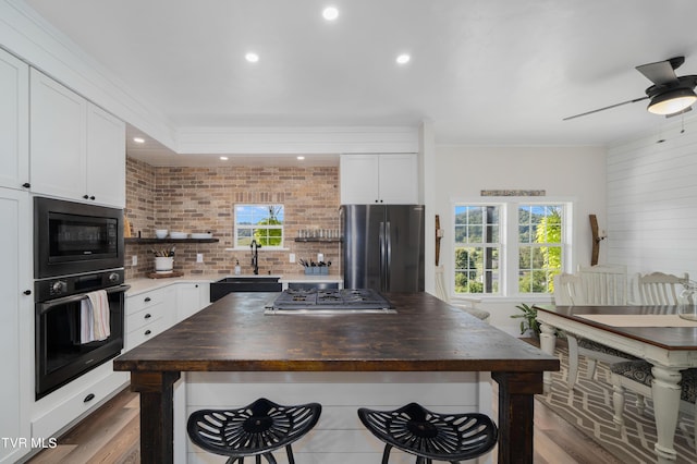 kitchen with sink, white cabinets, a center island, wooden counters, and black appliances