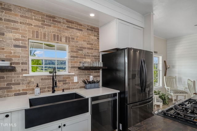 kitchen with dishwasher, brick wall, stainless steel fridge, white cabinets, and sink