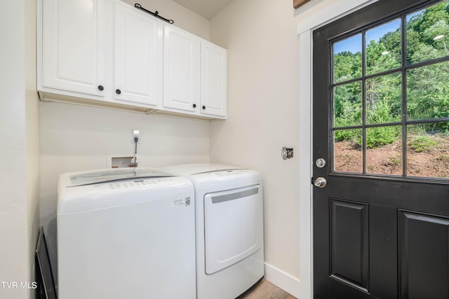 laundry area with washing machine and clothes dryer, cabinets, and light hardwood / wood-style flooring