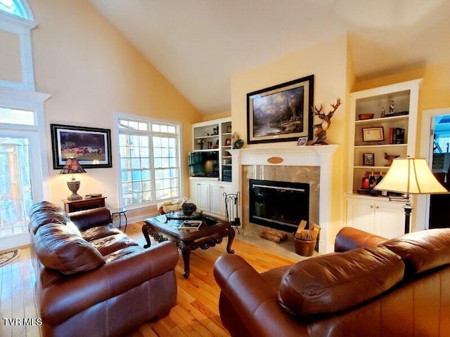 living room featuring light hardwood / wood-style floors, a premium fireplace, a high ceiling, and built in shelves