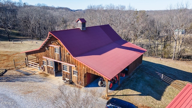 exterior space with a barn, an exterior structure, a forest view, an outdoor structure, and metal roof