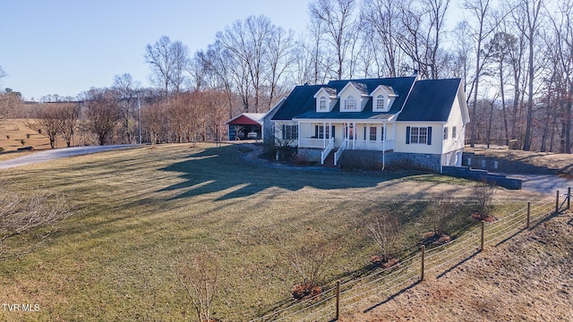 new england style home featuring driveway, covered porch, a front lawn, and fence