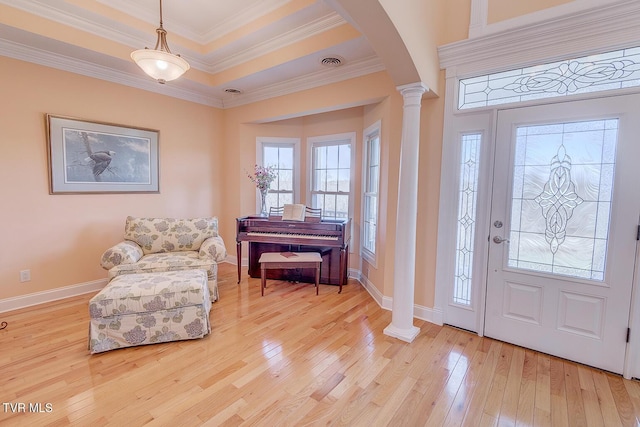 entrance foyer with a tray ceiling, crown molding, light hardwood / wood-style floors, and ornate columns