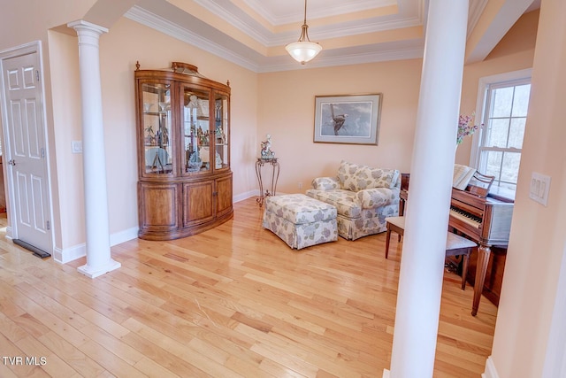 living area featuring light wood-style flooring, ornamental molding, a tray ceiling, decorative columns, and baseboards