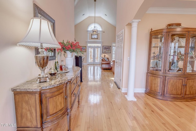 foyer entrance featuring baseboards, decorative columns, french doors, light wood-style floors, and high vaulted ceiling