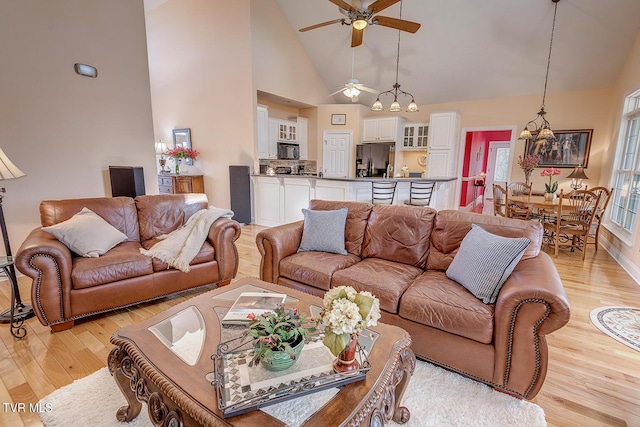 living room featuring ceiling fan, high vaulted ceiling, and light hardwood / wood-style flooring