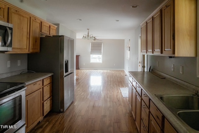 kitchen with hardwood / wood-style floors, ceiling fan with notable chandelier, sink, appliances with stainless steel finishes, and decorative light fixtures