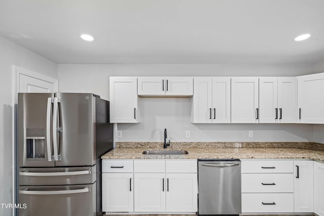 kitchen with light stone countertops, appliances with stainless steel finishes, white cabinetry, and sink