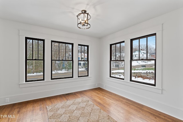 empty room featuring wood-type flooring and an inviting chandelier