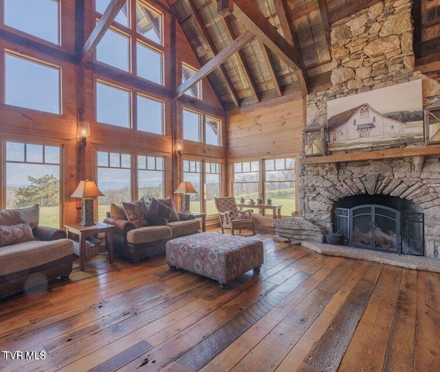 unfurnished living room with wood-type flooring, beamed ceiling, wooden walls, high vaulted ceiling, and a fireplace