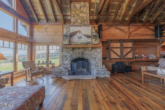 living room featuring wood walls, hardwood / wood-style floors, high vaulted ceiling, beam ceiling, and a stone fireplace