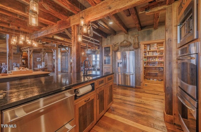 kitchen featuring stainless steel appliances, sink, beamed ceiling, wood walls, and pendant lighting