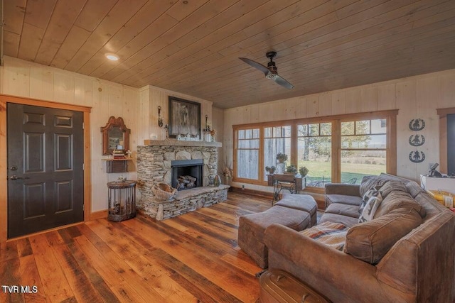 living room featuring ceiling fan, a stone fireplace, wooden ceiling, and wood-type flooring