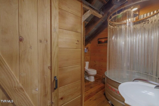 bathroom featuring lofted ceiling, hardwood / wood-style flooring, toilet, and wooden walls