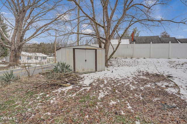 snow covered structure featuring fence, an outdoor structure, and a shed