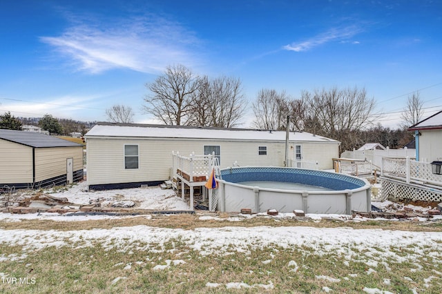 snow covered house featuring an outdoor pool, a wooden deck, and fence