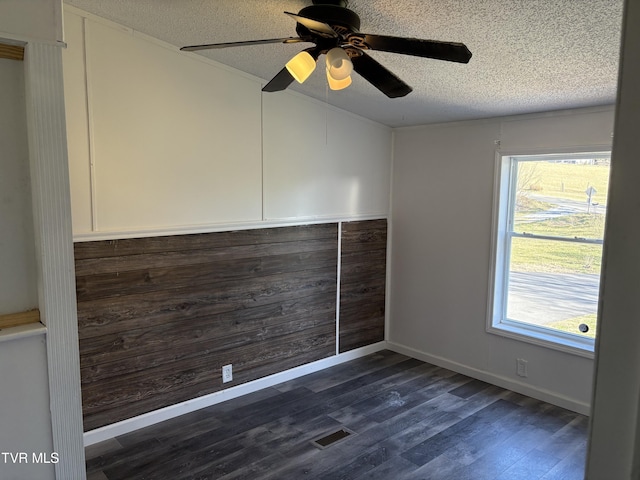 empty room with visible vents, plenty of natural light, a textured ceiling, and dark wood-style floors