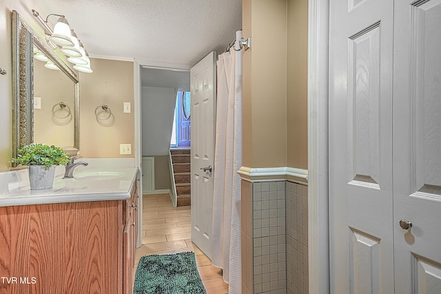 bathroom with tile walls, a textured ceiling, ornamental molding, and vanity